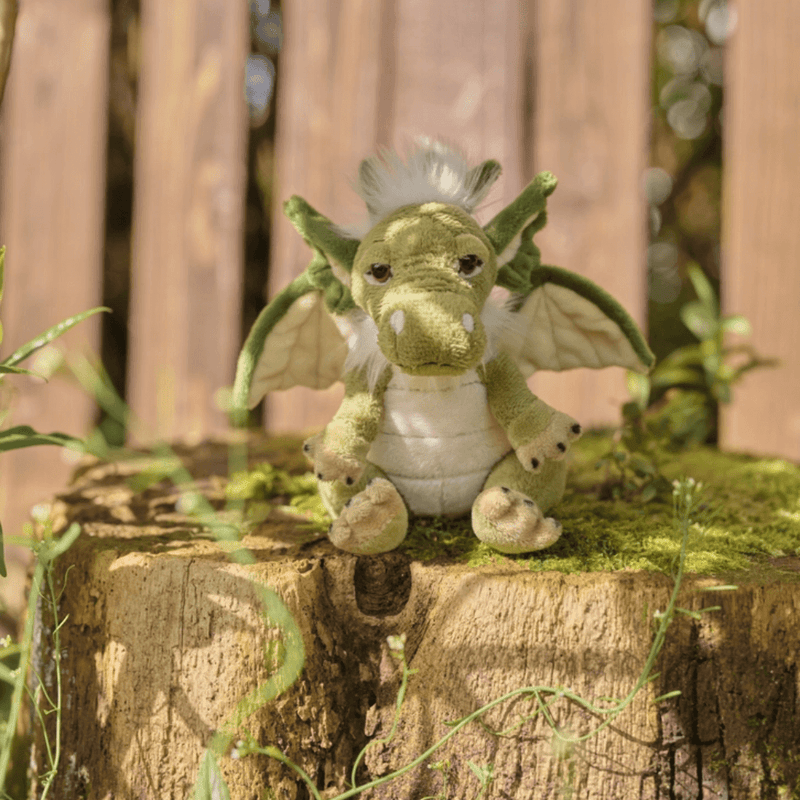 Signals green dragon plush by Charlie Bears Cuddle Cubs sitting on a mossy tree stump outdoors, small dragon soft toy