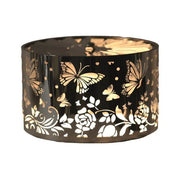 Silver butterfly and flower carousel candle shade glowing warmly above a lit jar candle.

