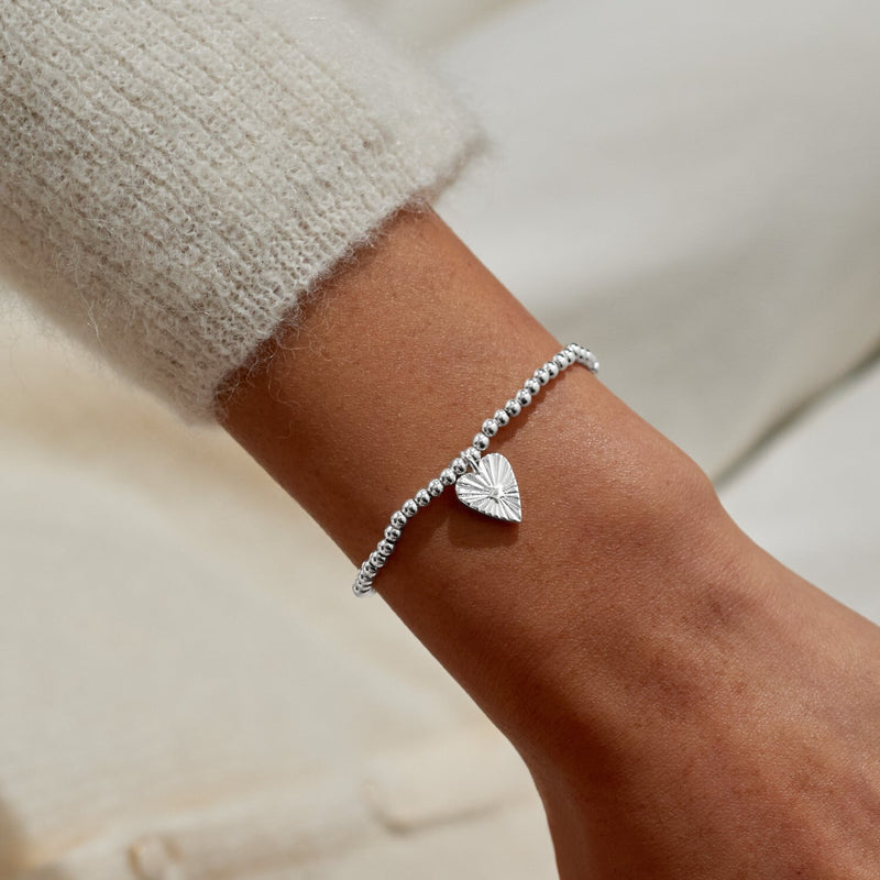 “Woman wearing silver beaded bracelet with sunburst heart charm – lifestyle close‑up”

