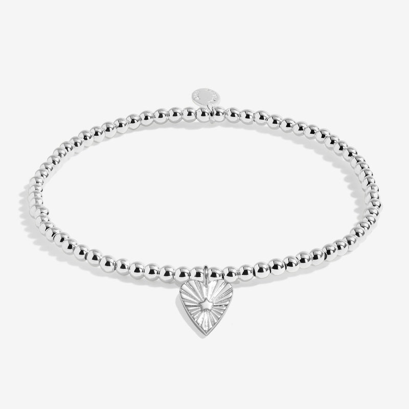 “Flat‑lay of silver‑plated beaded bracelet with sunburst heart charm”
