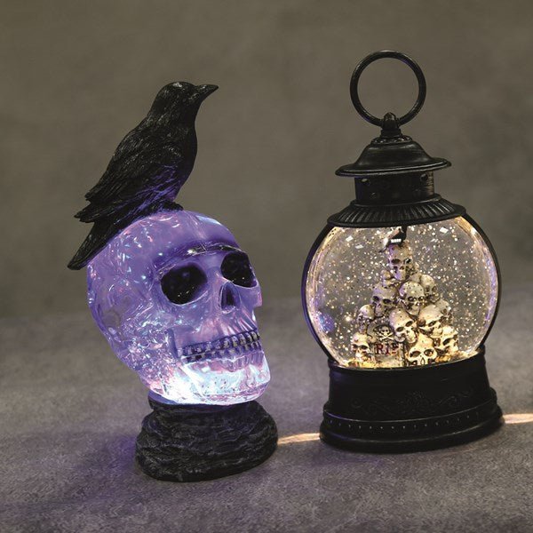 Lit skull water spinner with crow displayed on a surface beside a black lantern spinner, moody backdrop.