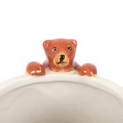 Close-up of 3-D bear figurine perched on rim of cream ceramic mug.
