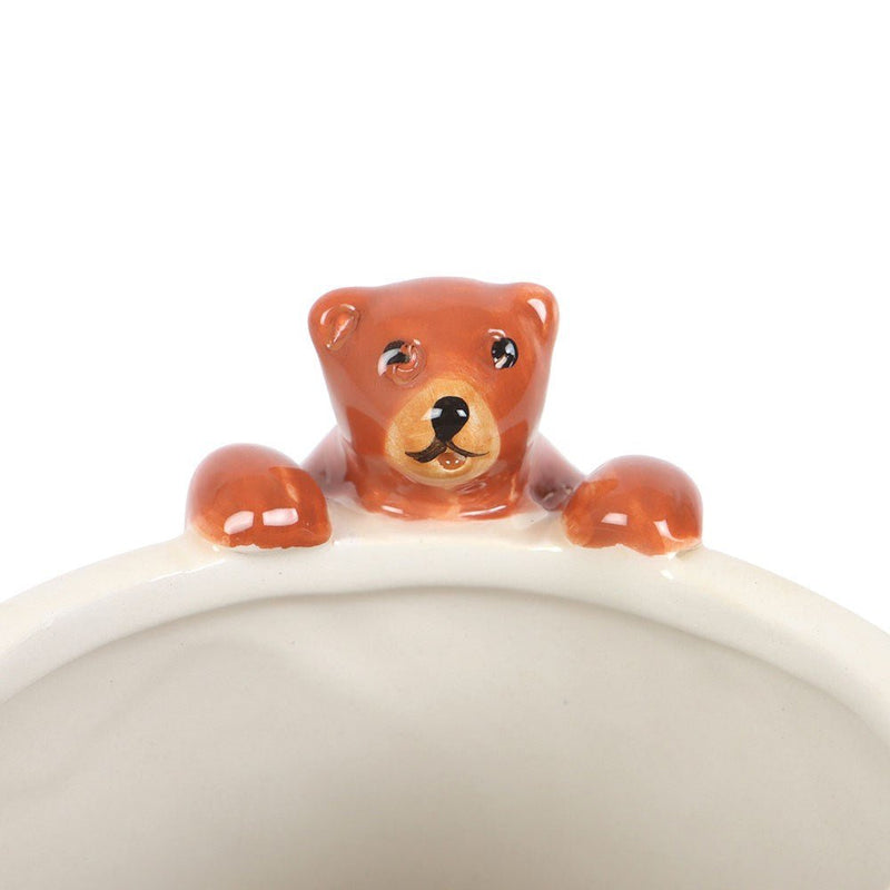 Close-up of 3-D bear figurine perched on rim of cream ceramic mug.
