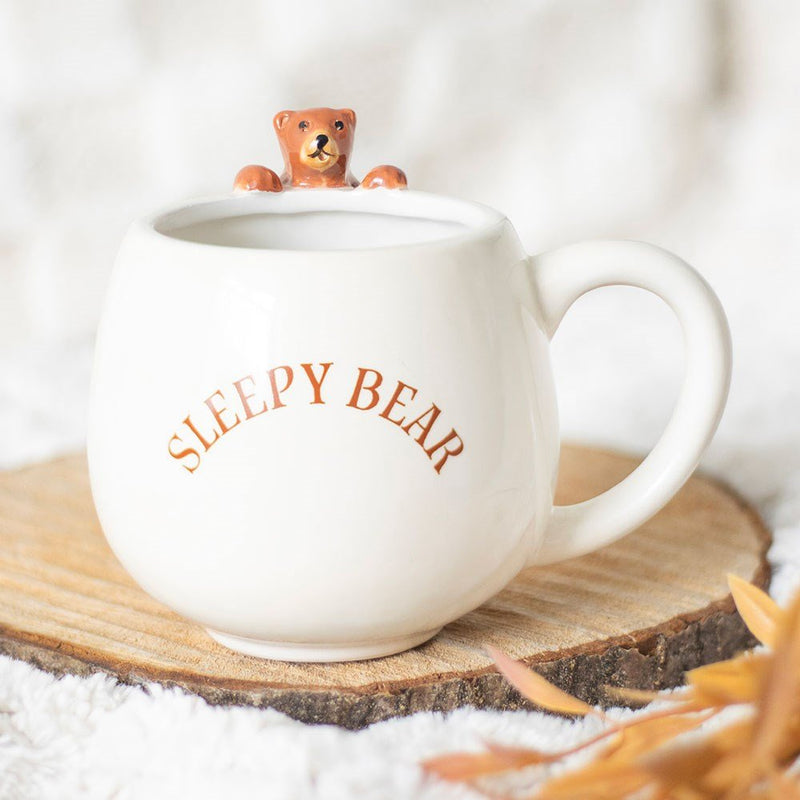 Cream ‘Sleepy Bear’ mug on rustic wood slice with bear figurine peeking over the rim.
