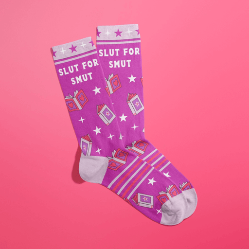 Overlapped purple women’s crew socks with lilac heels, toes and cuffs, white stars and pink book icons, slogan Slut For Smut, on pink background.