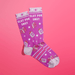Overlapped purple women’s crew socks with lilac heels, toes and cuffs, white stars and pink book icons, slogan Slut For Smut, on pink background.