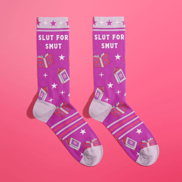Pair of purple women’s novelty crew socks with lilac accents, star pattern and cheeky Slut For Smut text with romance book graphics.