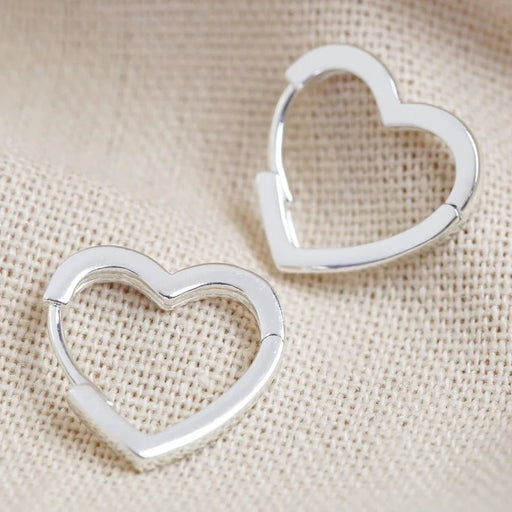 Close-up of small heart-shaped hoop earrings in polished silver on neutral fabric, minimal everyday huggies.