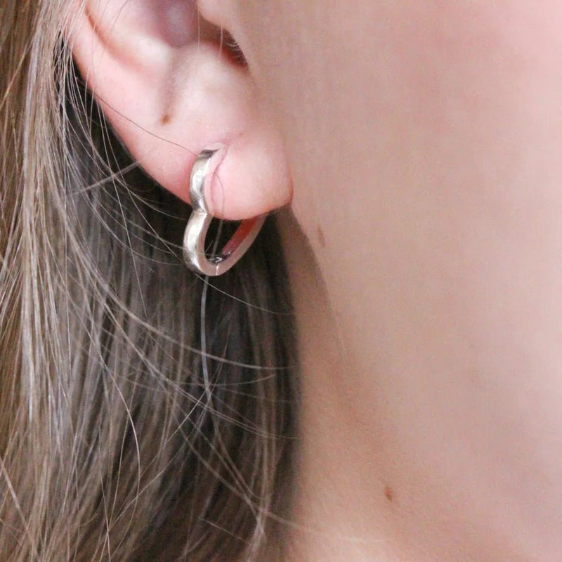 Small silver heart hoop worn in the lobe, neat huggie fit with smooth shine.