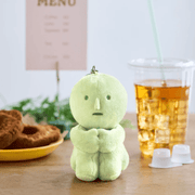 Smiski Hugging Knees green plush keyring sitting on a table