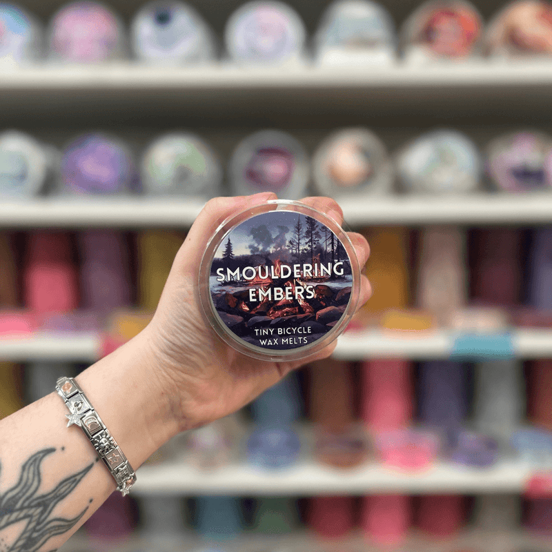 Smouldering Embers wax melt pot held in hand with colourful wax melt display in the background