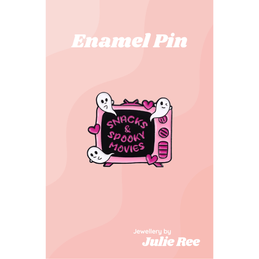 Pink and black enamel pin of a retro TV with cute ghosts, hearts, and the words Snacks & Spooky Movies, on a pink backing card.