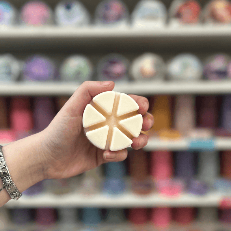 Solaris Blanc wax melt held in hand with a blurred display of colourful wax melts in the background