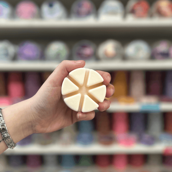 Solaris Blanc wax melt held in hand with a blurred display of colourful wax melts in the background