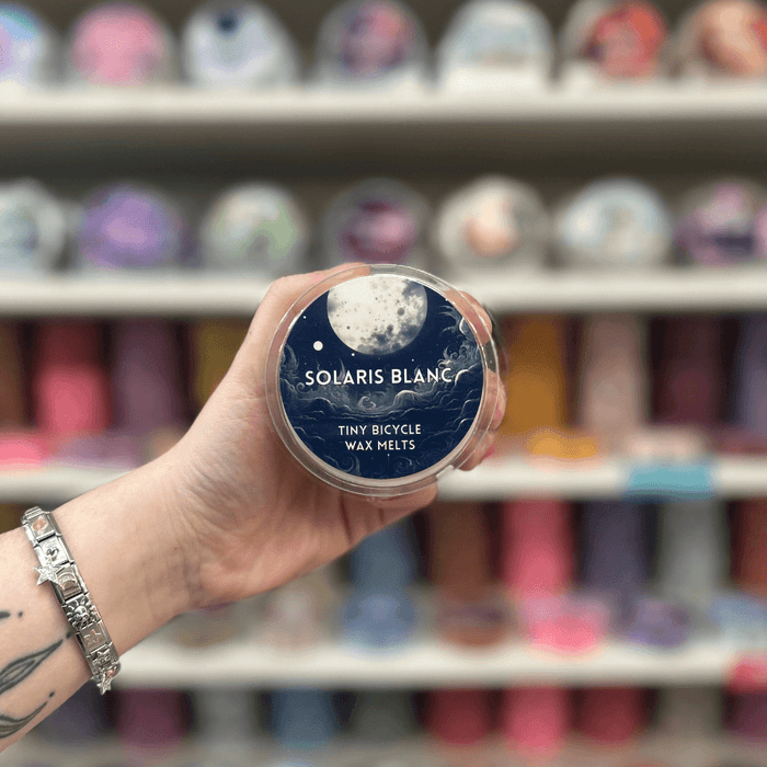 Solaris Blanc wax melt pot held in hand in front of a colourful wax melt display