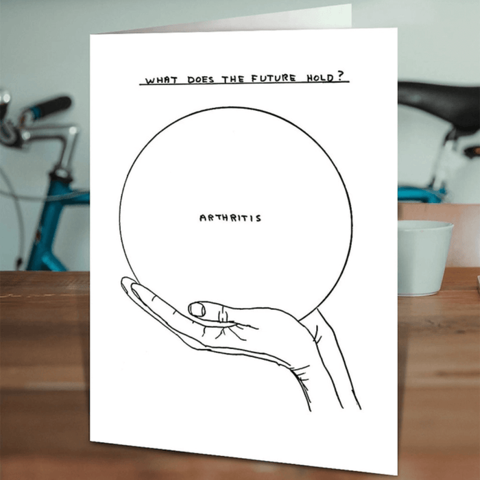 David Shrigley What does the future hold Arthritis card standing on a wooden table in a lifestyle setting.

