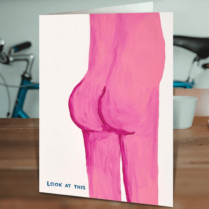 David Shrigley look at this pink bum card standing on a wooden table in a lifestyle scene.

