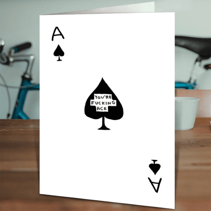 David Shrigley “You’re Fucking Ace” card on a wooden table in a lifestyle scene.

