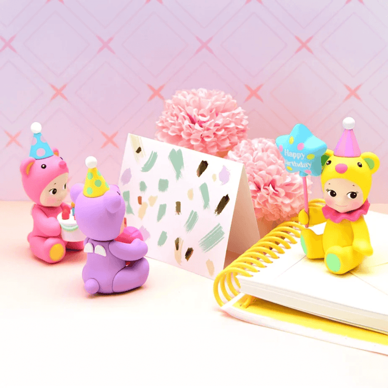 Pink, purple and yellow Sonny Angel Birthday Gift Bear figures displayed with a birthday card