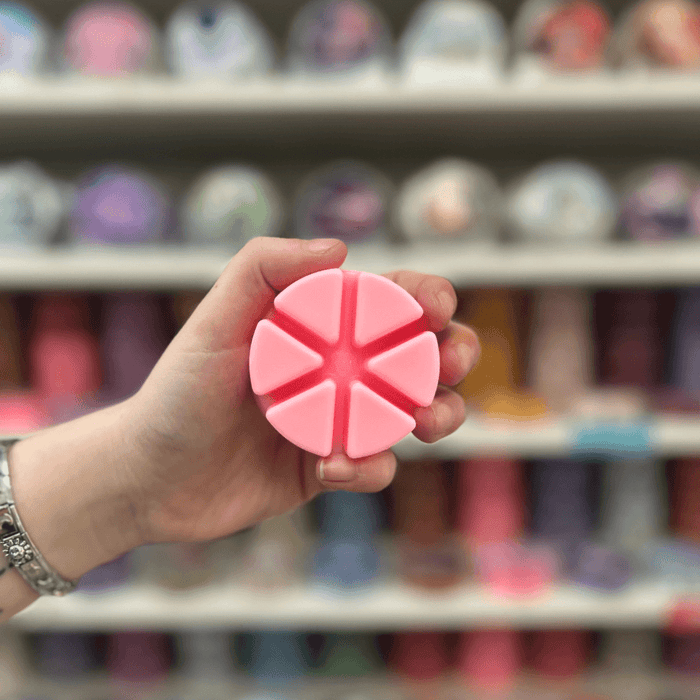 Pink segmented wax melt held in hand with a colourful wax melt display in the background
