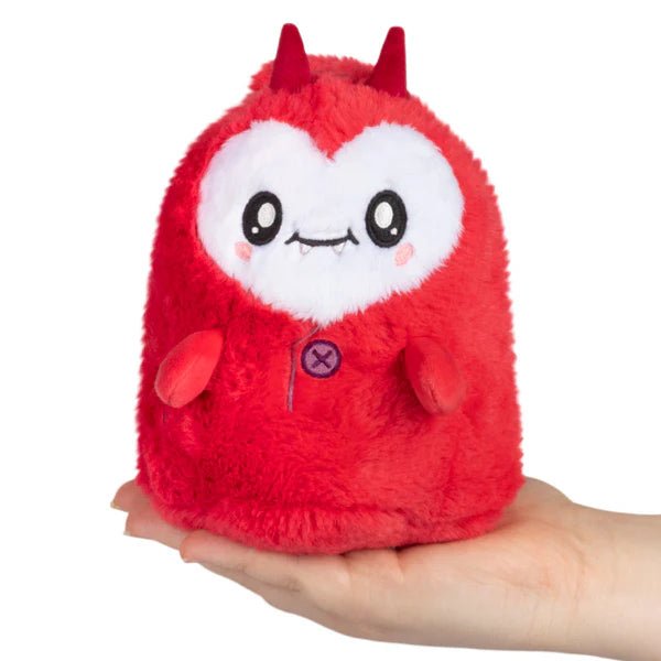 Front view of red Squishable Alter Egos Ghost Imp plush with heart-shaped white face and tiny fangs, held in hand