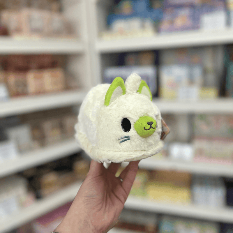 Squishable Alter Egos Ghost Kitty plush toy held in store, showing its cream fluffy body, green face details and cute spooky design