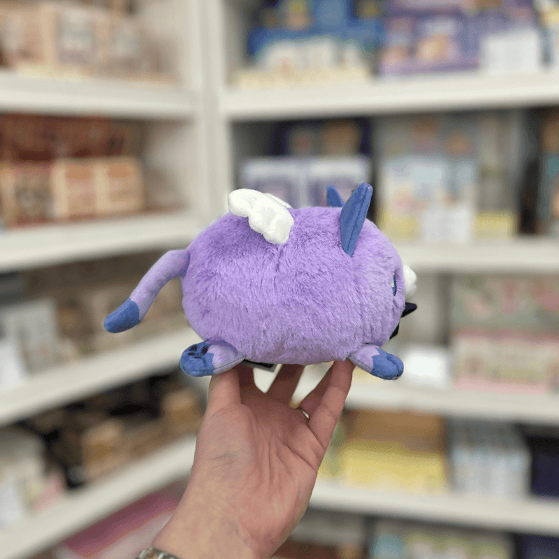 Side view of Squishable Alter Egos Magical Kitty plushie with purple fur, blue paws, little wings and a curled tail