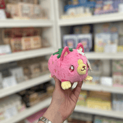 Squishable Alter Egos Strawberry Kitty plush toy held in store, showing its pink strawberry design, cat ears and green leafy detail