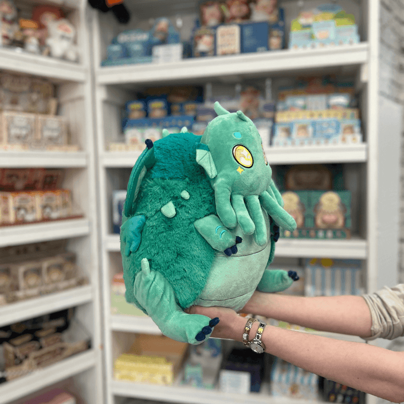 Squishable Baby Cthulhu plush toy held in hands in a gift shop, angled side view