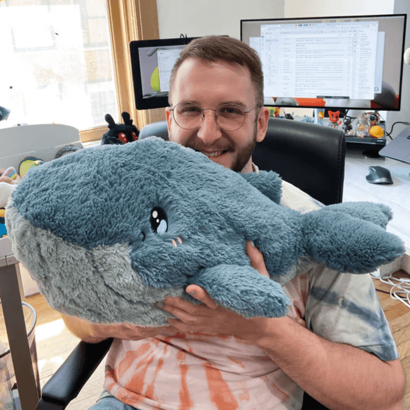 Person holding the Squishable Blue Whale plush toy to show its large, cuddly size