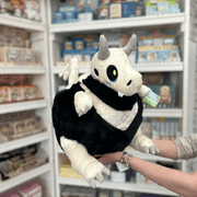 Squishable Bone Dragon plush toy held in hands in a gift shop, angled side view