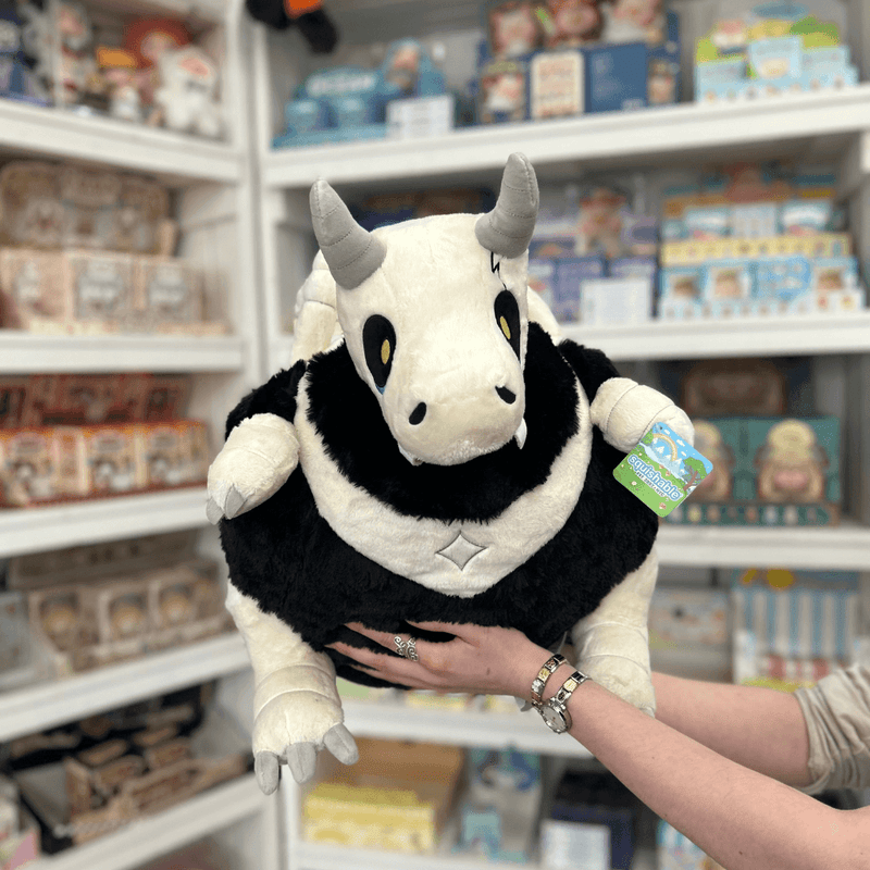 Squishable Bone Dragon plush toy held in hands in a gift shop, front view
