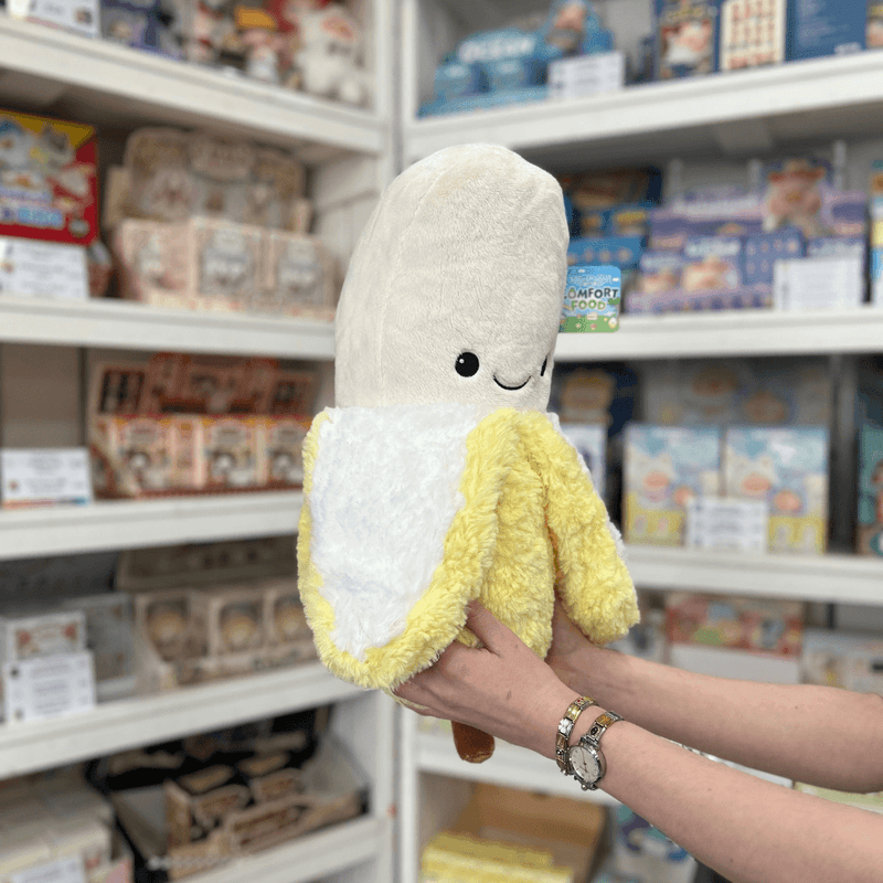 Squishable Comfort Food Banana plush toy angled view held in hands in a shop