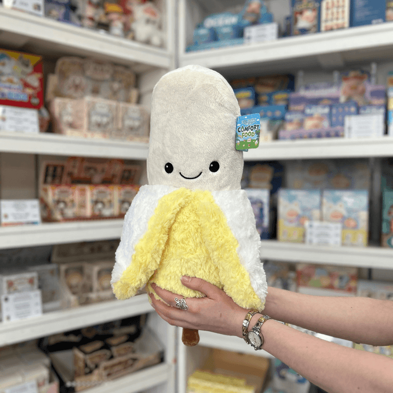 Squishable Comfort Food Banana plush toy front view held in hands in a shop