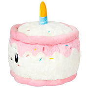 Side view of the Squishable Birthday Cake plushie with layered white and pink icing and a soft flame-topped candle.