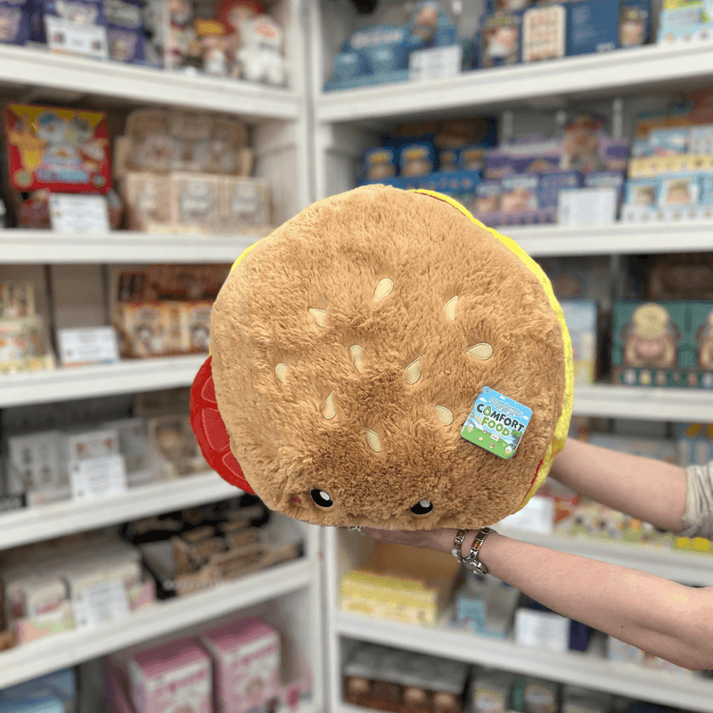 Squishable Comfort Food Cheeseburger plush toy held in hands in a gift shop, top view showing sesame seed bun