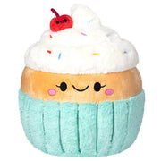 Front view of the Squishable Madame Cupcake plushie with a smiling face, whipped topping, rainbow sprinkles, and a red cherry.
