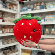Squishable Comfort Food Strawberry plush toy held in hands in a gift shop, angled side view