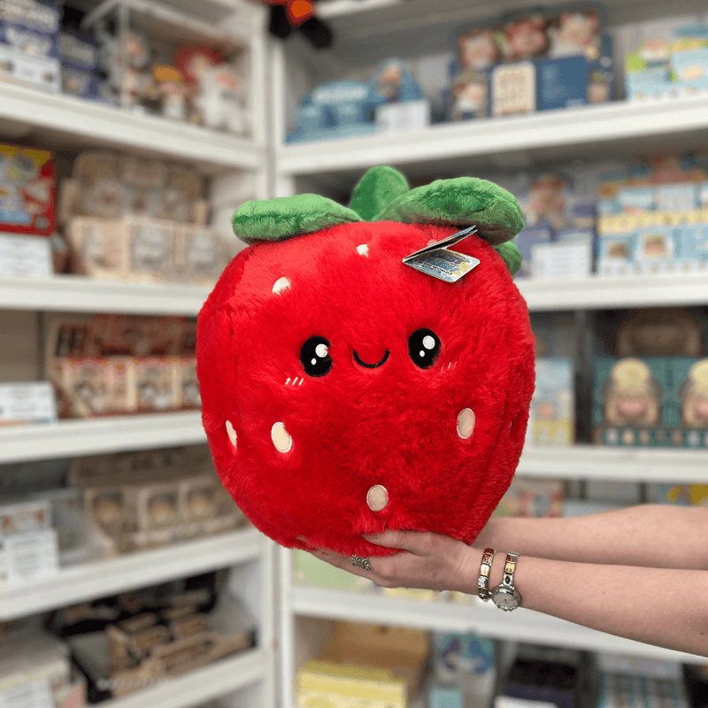Squishable Comfort Food Strawberry plush toy held in hands in a gift shop, front view