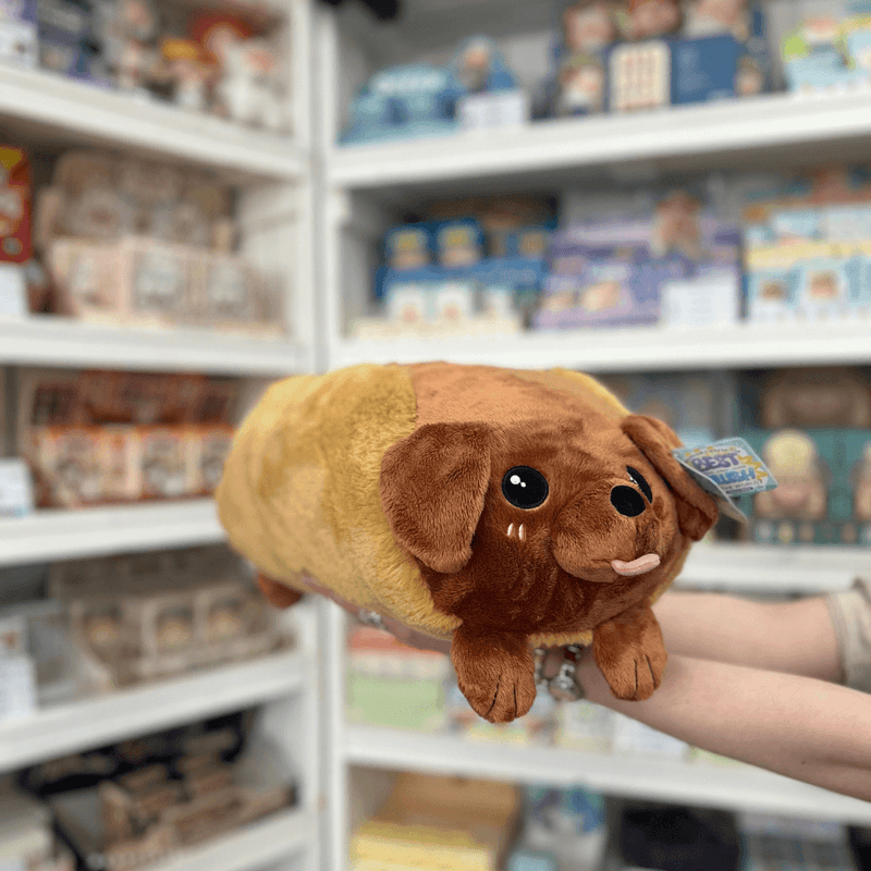 Squishable Dachshund Hot Dog plush toy angled view held in hands in a shop