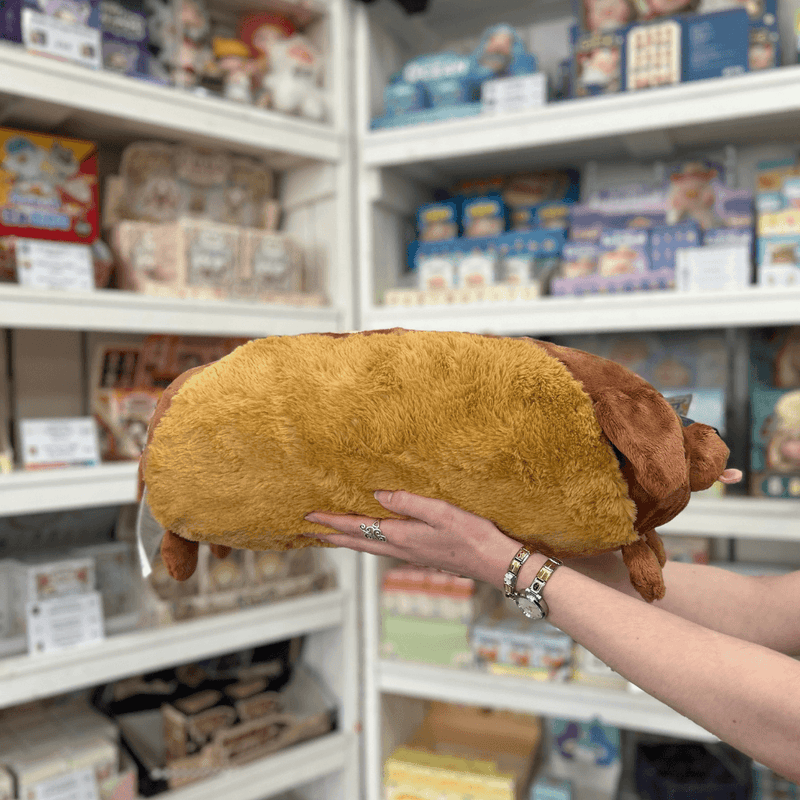 Squishable Dachshund Hot Dog plush toy side view held in hands in a shop