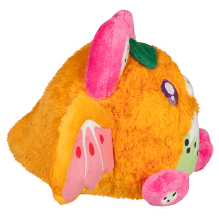 Side view of Mini Squishable Fruit Bat plush showing pink wings and fuzzy orange fur