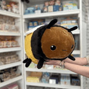 Squishable Fuzzy Bumblebee plush toy held in hands in a gift shop, angled side view