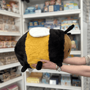 Squishable Fuzzy Bumblebee plush toy held in hands in a gift shop, side view