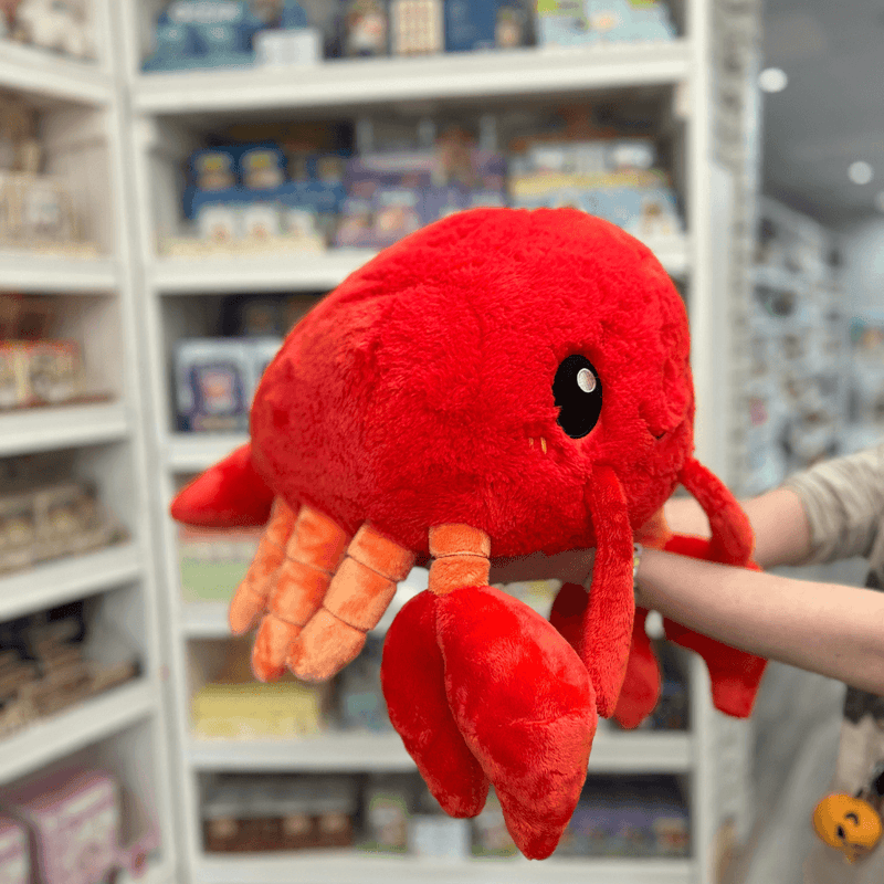 Squishable Lobster plush toy held in hands in a gift shop, angled side view