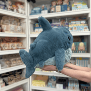 Squishable Megalodon plush toy held in hands in a gift shop, back view showing tail and fins