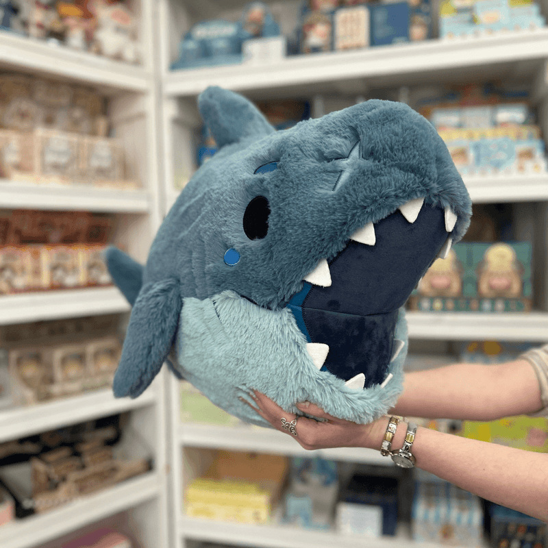 Squishable Megalodon plush toy held in hands in a gift shop, front view with open mouth