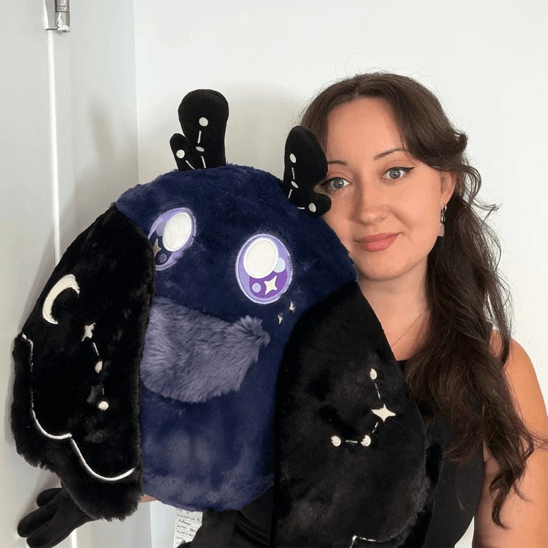 Person holding Squishable Midnight Mothman plush showing its large midnight-blue body and celestial wings