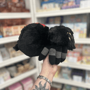 Mini Squishable Black Widow plush toy held in hand in a gift shop, back view