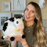 Person holding Squishable Mini Cow plush toy with black and white patches and jingle bell collar